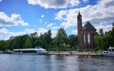 Boot auf dem Wasser mit Kirche im Hintergrund, bei schönem Wetter.